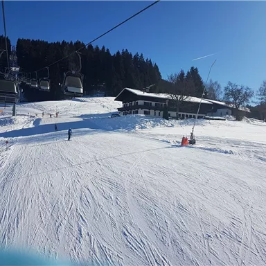 Eine schöne Winterlandschaft mit schneebedeckten Pisten und einem Skilift. Im Hintergrund ist ein gemütliches Skihütten.