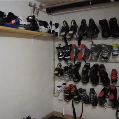 A room with various ski and snowboard boots neatly hanging on a wall. Above is a shelf with additional pairs of shoes.