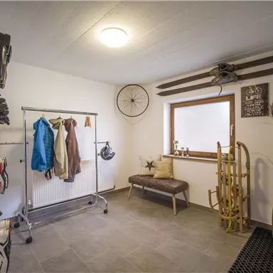 A well-organized ski room with ski equipment and hanging options for clothing. The walls are bright and there is a window that provides natural light.