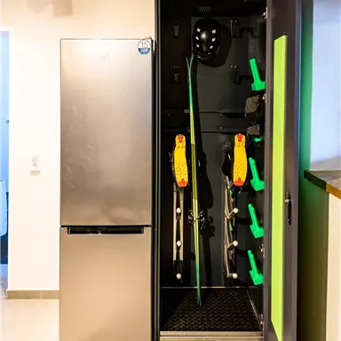 A modern ski room with a refrigerator and equipment storage. Skis, helmets, and ski rollers are neatly organized.
