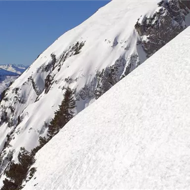 Ein schneebedeckter Berg mit einem klaren blauen Himmel. Eine Person klettert an einer steilen Schneefläche.