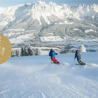 Zwei Skifahrer fahren eine verschneite Piste hinunter, umgeben von beeindruckenden Bergen. Der Himmel ist klar und die Landschaft ist wunderschönen Winterzauber.