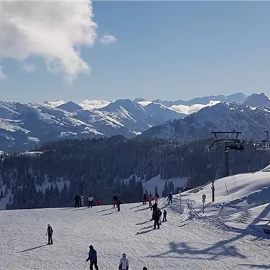 Eine schneebedeckte Berglandschaft mit Skifahrern und einem blauen Himmel. Im Hintergrund sind majestätische Berge zu sehen.