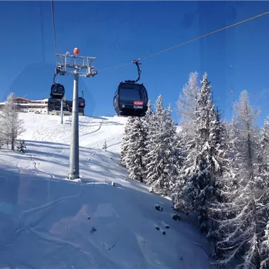 Eine Skilift-Gondel fährt über eine schneebedeckte Landschaft. Die Bäume sind mit Schnee bedeckt und der Himmel ist blau.