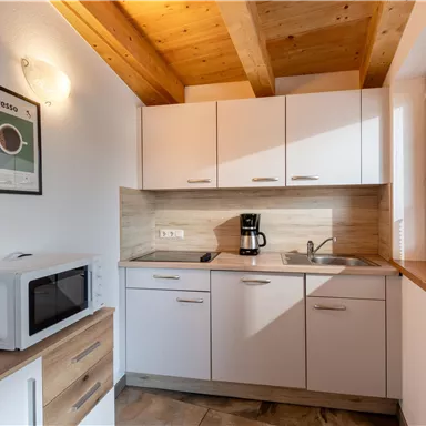 Eine moderne Küche mit Holzdetails und hellen Schränken. Auf der Arbeitsfläche stehen eine Kaffeemaschine und eine Mikrowelle.