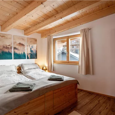 Ein gemütliches Schlafzimmer mit zwei Betten aus Holz und natürlichen Akzenten. Große Fenster bringen viel Licht in den Raum.