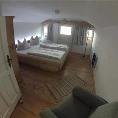 A cozy bedroom with two single beds and wooden flooring. The windows let in plenty of daylight, and there is a small seating area.