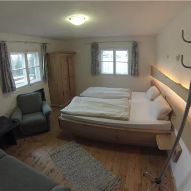 A cozy bedroom with two beds and a small seating area. There are windows that provide plenty of natural light.