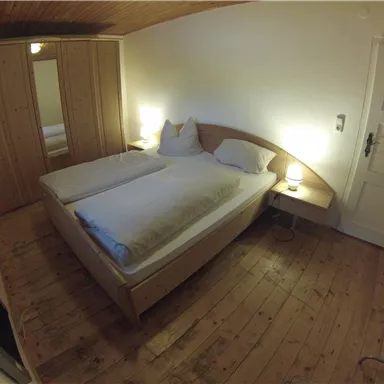 A cozy bedroom with two beds and wooden flooring. There is a wardrobe and a cozy bedside lamp.