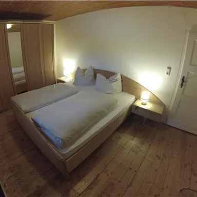 A cozy bedroom with a double bed and wooden flooring. There is a wardrobe and soft lighting.
