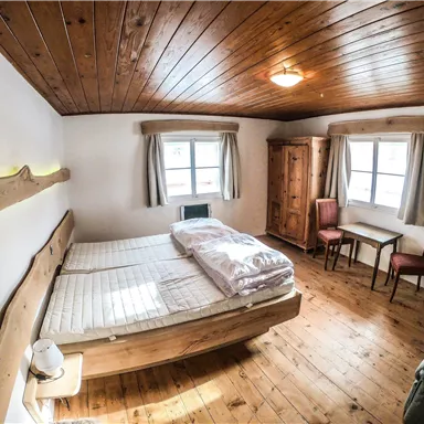 A cozy bedroom with a wooden ceiling and a large bed. There is a table, two chairs, and a wardrobe.