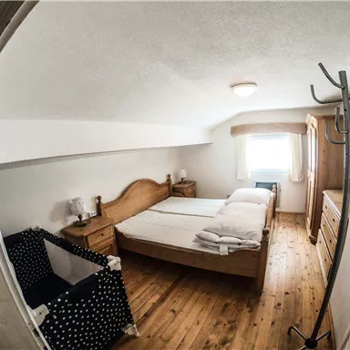 A bright bedroom with two beds and wooden flooring. There is a wardrobe and a cozy seating area.