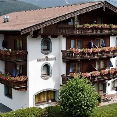 Ein traditionelles alpenländisches Gebäude mit Blumenkästen an den Balkonen. Umgeben von grünen Gärten und Bergen im Hintergrund.
