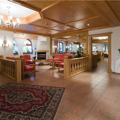 A cozy reception area with wooden furniture and red seating. The room is brightly lit and features a fireplace as well as plants.