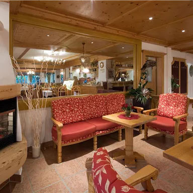 A cozy seating area with red upholstered furniture and a fireplace. In the background, an inviting restaurant atmosphere can be seen.