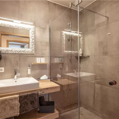 A modern bathroom with a glass shower and a stylish sink. The walls are in neutral gray tones, and a decorative mirror completes the design.
