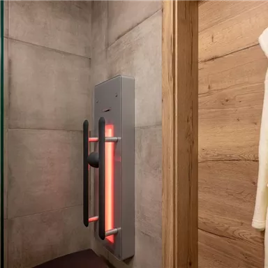 A modern bathroom with a shower cabin and an infrared heater. A white bathrobe hangs on the wall.