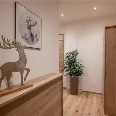 A stylish hallway with a wooden piece of furniture and a decorative deer figure. An artwork featuring a deer motif hangs on the wall and a plant stands in the corner.