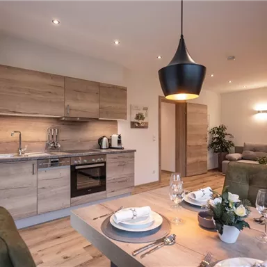 A modern kitchen with wooden fronts and appliances in an open living area. The table is beautifully set with dishes and glasses, and a cozy seating area invites you to relax.