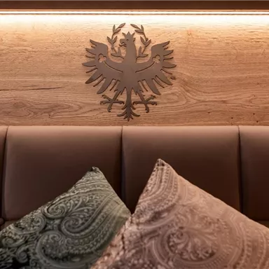 A stylish headboard with a coat of arms in the background. Elegant cushions in soft colors are lying on the bed.