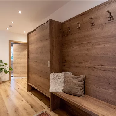 A bright hallway with wooden furniture and a cozy bench. A plant and a rug create an inviting atmosphere.