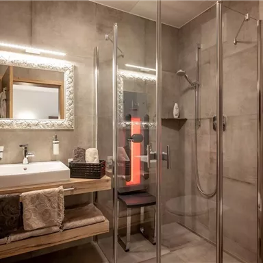 A modern bathroom with shower and sink. The walls are in neutral tones, and there is a large mirror lighting.