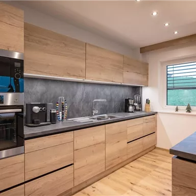 A modern kitchen with wooden surfaces and stainless steel appliances. The window lets in plenty of daylight and offers a view of the greenery.