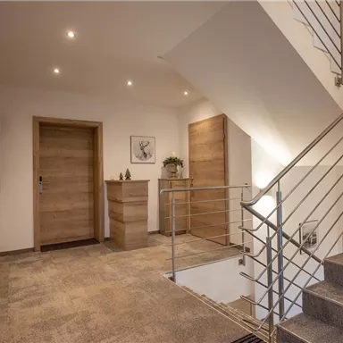 A bright entrance area with stairs and modern wooden doors. The walls are simple and the lighting is friendly.