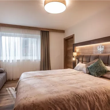 A cozy bedroom with a large bed and warm colors. Bright windows create an inviting atmosphere.