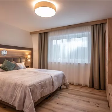 A modern bedroom with a large bed and soft color tones. Daylight streams through the window, creating a bright atmosphere.