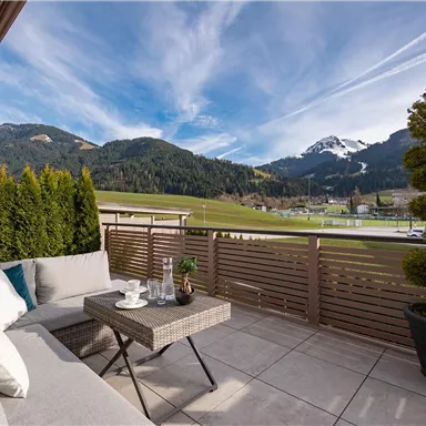 A cozy terrace with an elegant seating area and a table. In the background, picturesque mountains and a clear sky can be seen.