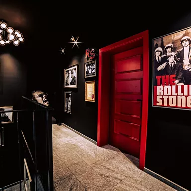 A stylish hallway with black walls and a red door. Pictures hang on the walls, including a famous poster of The Rolling Stones.