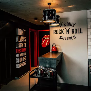 A modern kitchen with rocky decoration and a striking red refrigerator. On the walls are creative sayings that convey a musical flair.