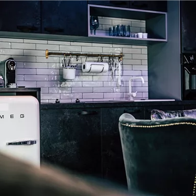 A modern kitchen featuring a SMEG refrigerator and stylish kitchen cabinets. The walls are designed with white tiles and approximately wooden accents.