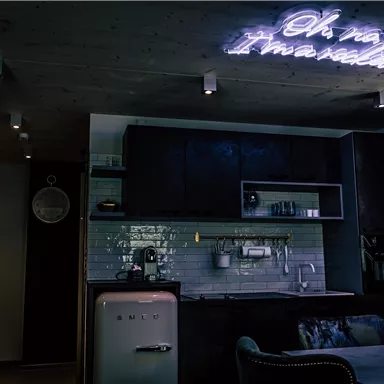 A modern kitchen with stylish furnishings and a neon-lit wall decor. The atmosphere is cozy and inviting.
