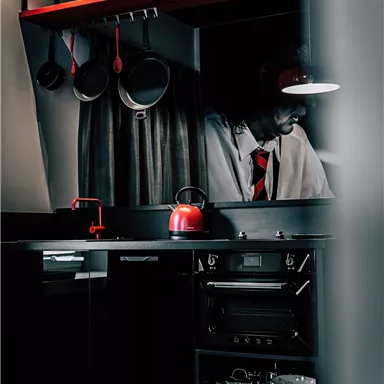 A modern kitchen in black and red with pots and a red coffee pot. The decor is stylish and elegant.
