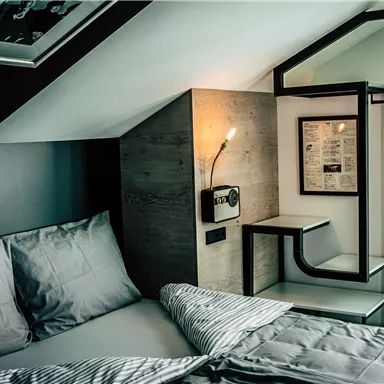 A modern bedroom with a large bed and minimalist decor. The walls are painted in neutral colors and a lamp provides cozy light.