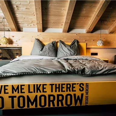 A modern bedroom with a large bed and a unique yellow bed trim. The cozy atmosphere is emphasized by wooden accents and soft lighting.