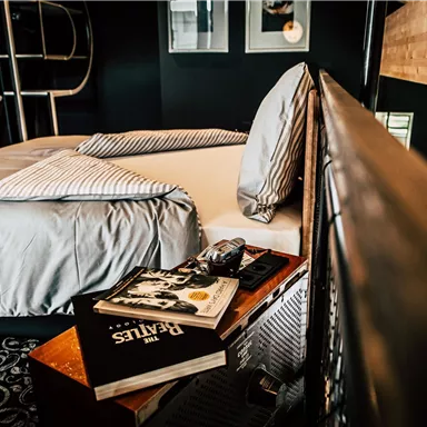 A stylish bedroom with a modern bed and decorative pillows. Next to the bed, a few books are lying on a wooden tray.
