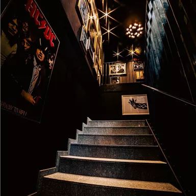 A stylish staircase with stone steps leads into a dark corridor. Decorative pictures hang on the walls and the lighting is dim.