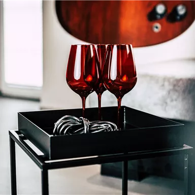 Three red wine glasses are standing on a black tray. Next to it lies a knotted cable.