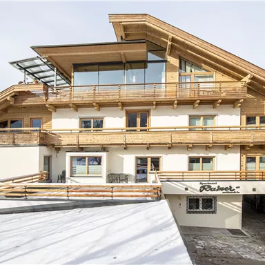 Ein modernes Gebäude mit Holzverkleidung und großen Fenstern. Die Konstruktion zeigt einen alpinen Stil und liegt in einer schneebedeckten Umgebung.