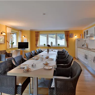 Eine moderne Küche mit einem großen Esstisch und stilvollen Stühlen. Helle Wände und Fenster sorgen für eine freundliche Atmosphäre.