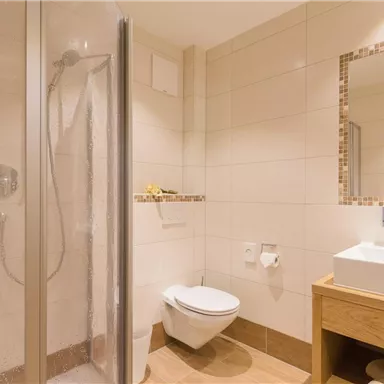 Ein modernes Badezimmer mit einer Dusche und einem Waschbecken aus Holz. Es bietet helle Wände und eine schnörkellose Ausstattung.