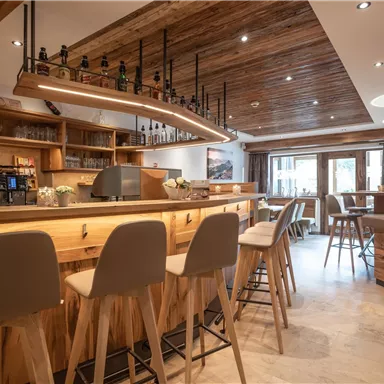 Eine gemütliche Bar mit Holzregalen und modernem Interieur. Helle Beleuchtung schafft eine einladende Atmosphäre.