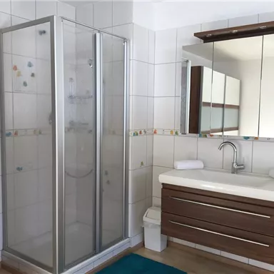 A modern bathroom with a shower and an elegant sink. The tiles are bright and the decor is simple and stylish.