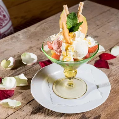 Ein verführerisches Eisbecher mit verschiedenen Eissorten, Sahne und frischen Früchten. Umgeben von Rospetalen auf einem Holztisch.