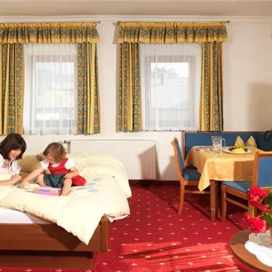 Ein gemütliches Hotelzimmer mit einem Doppelbett und einem Tisch. Eine Mutter liest mit ihrem Kind auf dem Bett.