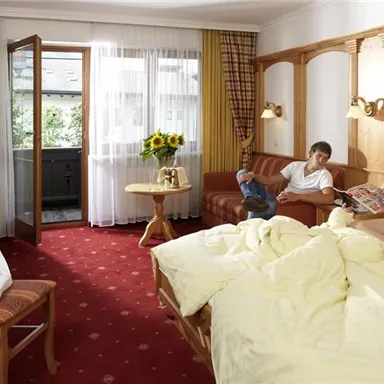 Ein gemütliches Hotelzimmer mit einem großen Bett und einem Sofa. Zwei Personen entspannen sich und genießen die Umgebung.