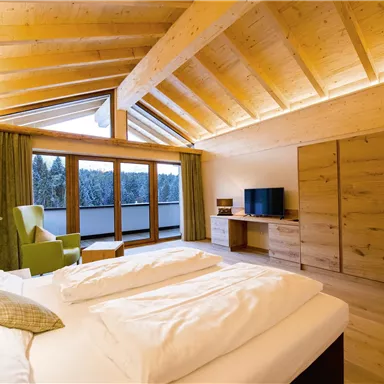 Ein modernes Schlafzimmer mit Holzdecken und einem großen Fenster. Das Zimmer ist hell und gemütlich eingerichtet.